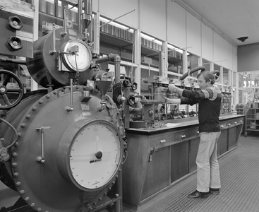 883646 Afbeelding van een monteur van de R.E.M.U. tijdens werkzaamheden aan een gasmeter in de werkplaats van de ...